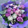 Hand-tied bouquet of lavender, pink, and white roses with accent flowers wrapped in purple paper.