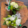 Pair of white and green floral boutonnieres with ribbons displayed on a rustic wood slice