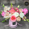 Pink and cream roses with mixed blooms arranged in a round pink hatbox-style container.