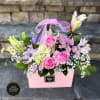 Pink gift bag of mixed flowers including pink roses, lilies, daisies, and filler with a sheer pink bow.