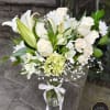 Tall white flower arrangement in a clear glass vase with a white ribbon bow