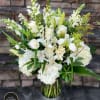 Tall arrangement of white roses, lilies, hydrangeas, and snapdragons in a clear glass vase.