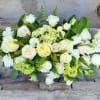Low arrangement of white and cream roses with soft green blooms in an elongated design