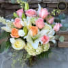 Glass vase arrangement of pink and peach roses with white lilies and hydrangea