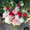 Arrangement of red and pink roses with white lilies and hydrangeas in a textured glass vase