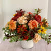 Mixed autumn bouquet in a white vase with orange, red, yellow, and cream blooms