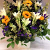 Bouquet of white lilies, sunflowers, and purple flowers in a white vase