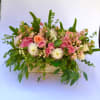 Pink and peach roses in a low wooden container with greenery