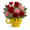 Red roses and pink carnations in a yellow smiley-face mug