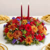 Red and orange floral centerpiece with two burgundy taper candles