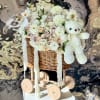 White floral basket arrangement with a teddy bear on a wooden cart