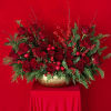 Red roses arranged in a gold vase with evergreen accents and red berries
