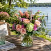 This enchanting floral arrangement blends soft peach hues with delicate greens and