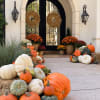 Fall porch display with pumpkins, mums, and wreaths by a front door