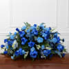 A graceful casket spray arranged in soothing shades of blue, complemented by