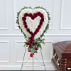 Heart-shaped funeral spray of white flowers and red roses beside a casket
