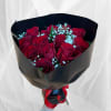 Handheld bouquet of red roses with white filler wrapped in black paper and red ribbon.