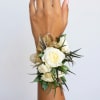 White rose wrist corsage with gold ribbon and greenery on a wrist