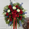 Large red, white, and blue funeral spray beside a casket