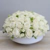 Low dome arrangement of cream white roses tightly packed in a round white bowl