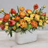 Rectangular white vase filled with yellow spray roses, orange ranunculus, and red-orange tulips.