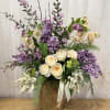 Tall floral arrangement with cream roses, purple blooms, and a woven basket vase