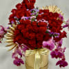 Red roses and purple orchids arranged in a gold box with ribbon
