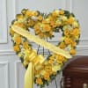 Yellow heart-shaped floral wreath with a sympathy ribbon on a stand