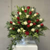 Red and white roses arranged in a white vase with lush greenery