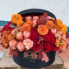 Orange pumpkins and red, peach, and orange flowers in a black hatbox