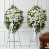 Two white funeral wreaths on stands beside a casket
