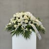 White floral funeral spray with lilies, roses, and orchids on a stand