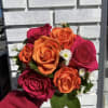 Handheld bouquet of orange and pink roses with small white daisies