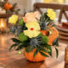 Pumpkin-shaped vase with yellow and peach flowers on a table
