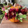 Floral arrangement in a pumpkin-shaped container with burgundy and white blooms