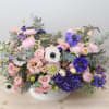 Pink and purple mixed flower arrangement in a white bowl vase