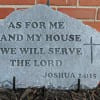 Engraved stone plaque with a Bible verse and cross against a brick wall