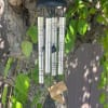 Silver wind chime hanging from a tree branch with green leaves