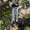 Decorative silver wind chime with blue butterflies and white flowers hanging from a tree branch