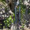 Black metal wind chime with memorial message hanging from a tree outdoors.