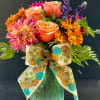 Colorful bouquet of roses, dahlias, and daisies in a green vase with a pumpkin ribbon