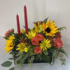 Flower arrangement with sunflowers, orange roses, and red candles in a black container