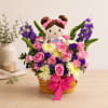 Basket arrangement with a doll surrounded by pink, purple, and white flowers