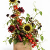 Mixed floral arrangement with sunflowers, dark daisies, berries, and tomatoes in a wooden box