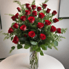 A dense cluster of long-stemmed red roses rises from a tall clear
