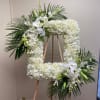 Large white floral wreath on an easel with palm fronds and orchids
