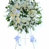 White floral standing wreath on an easel with blue ribbons
