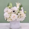 White floral arrangement in a white vase with lilies and roses