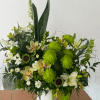Green and white floral arrangement in a white vase with orchids and lilies
