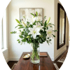 A cluster of large white lilies arranged upright in a tall clear